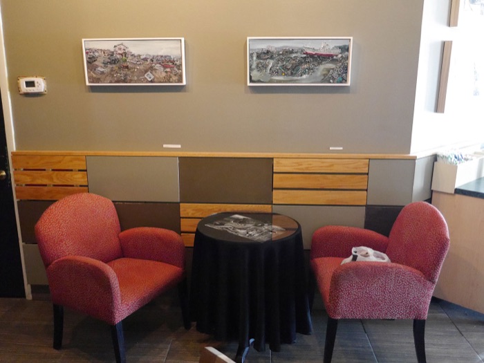 Two red armchairs by a small table under a pair of framed paintings