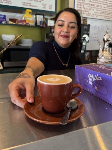 A barista sliding a cappuccino with heart latte art across the counter