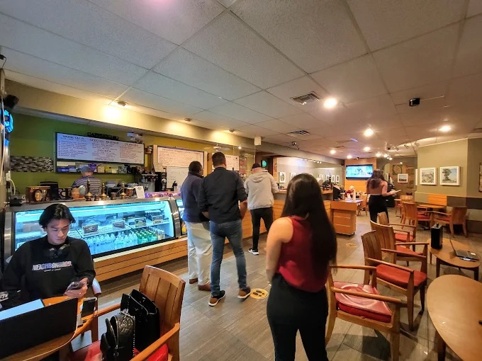 A line of customers at the counter beside the pastry case, with people at tables across the room