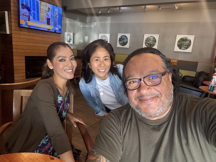 Three friends smiling for a selfie at a table under the round framed prints