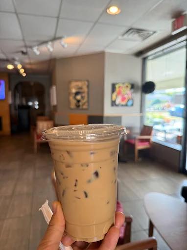 An iced coffee held up inside the shop, with art on the walls behind it