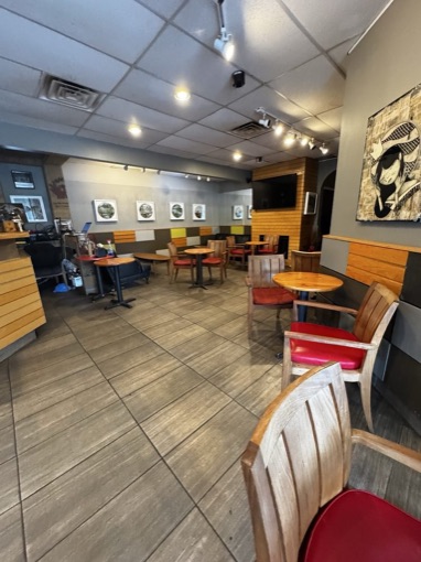 Wooden tables and red-cushioned chairs under a row of framed prints