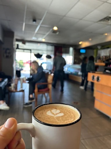 A latte with heart latte art held up in front of the busy dining room