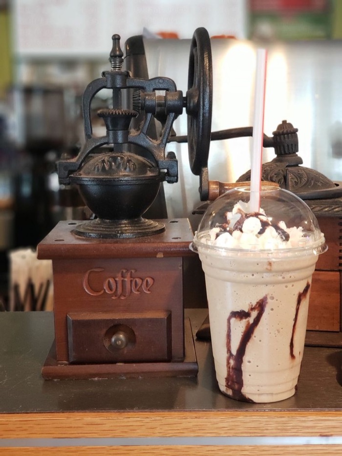 A frozen Kona Mocha with whipped cream next to an antique coffee grinder