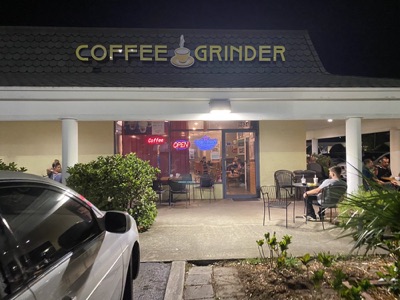 The Coffee Grinder storefront lit up at night, with people out on the patio