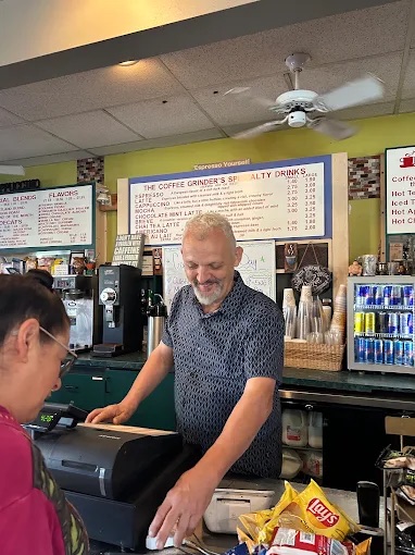 Smiling behind the register, with the specialty drinks board on the wall