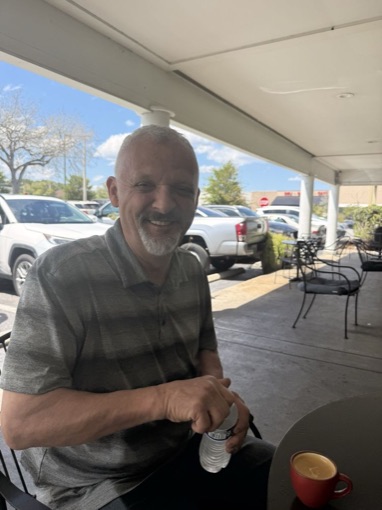 Slava smiling at a patio table with an espresso in a red cup